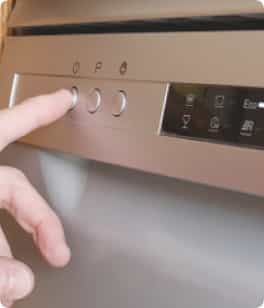 Persona presiona botón de una máquina lavavajillas de color gris